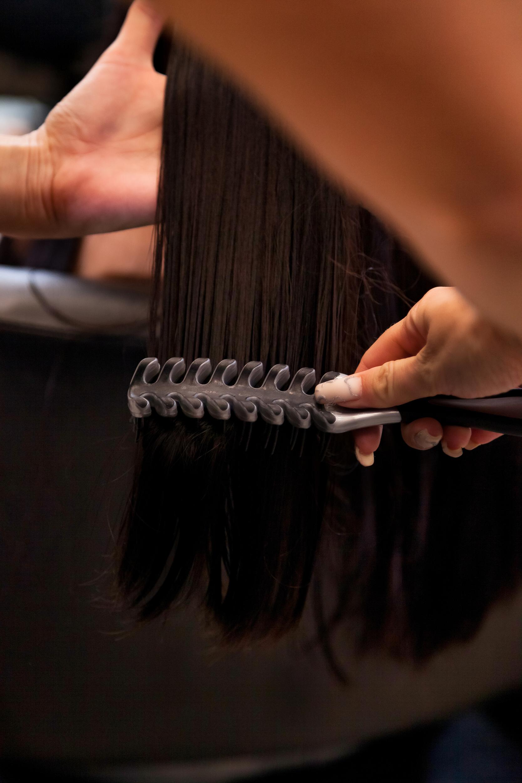 primer plano de manos de un estilista peinado eñ cabello con un peine